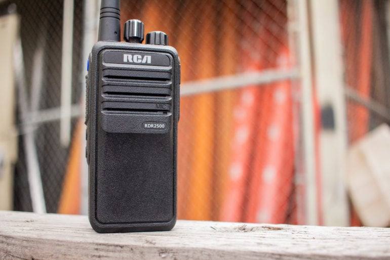 An RDR2500 handheld 2-way radio sits upright on a wood plank outside a construction zone.